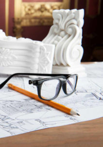 Closeup portrait of spectacles, yellow pencil, design drawing and white stucco moulding, on wooden table over classical interior at studio shot